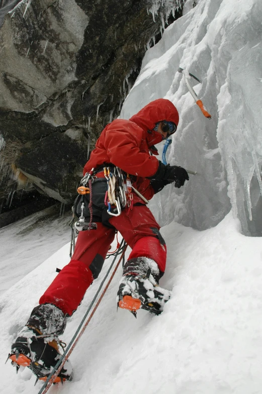skier in a red ski suit and full red snow pants climbing the side of a snowy mountain