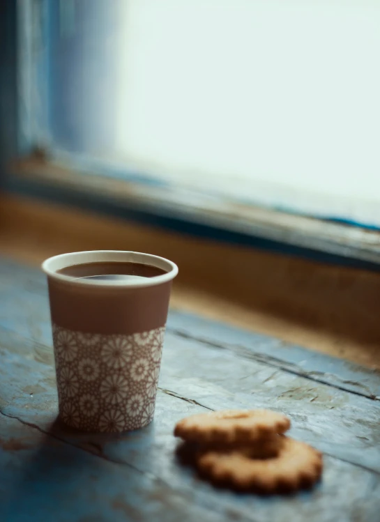 a cookie and cup on the table next to a window