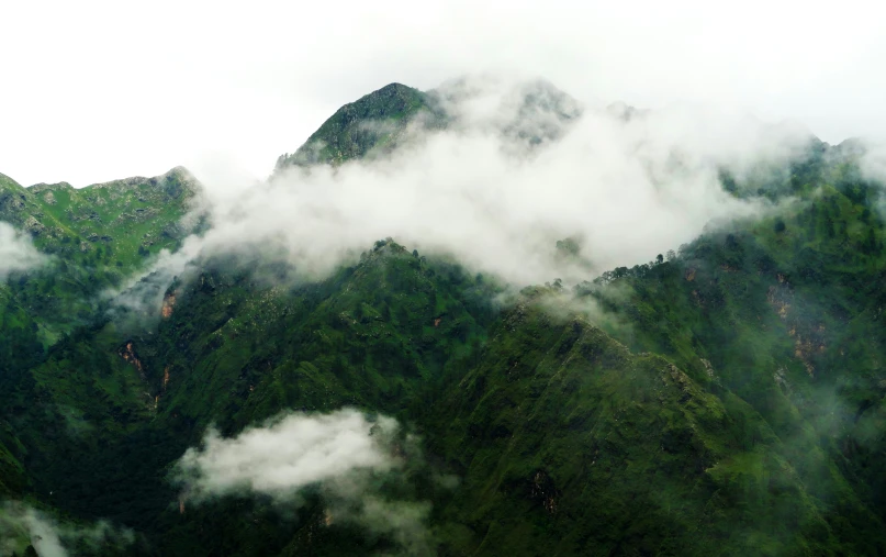 green mountains are obscured by clouds as they roll down the hill