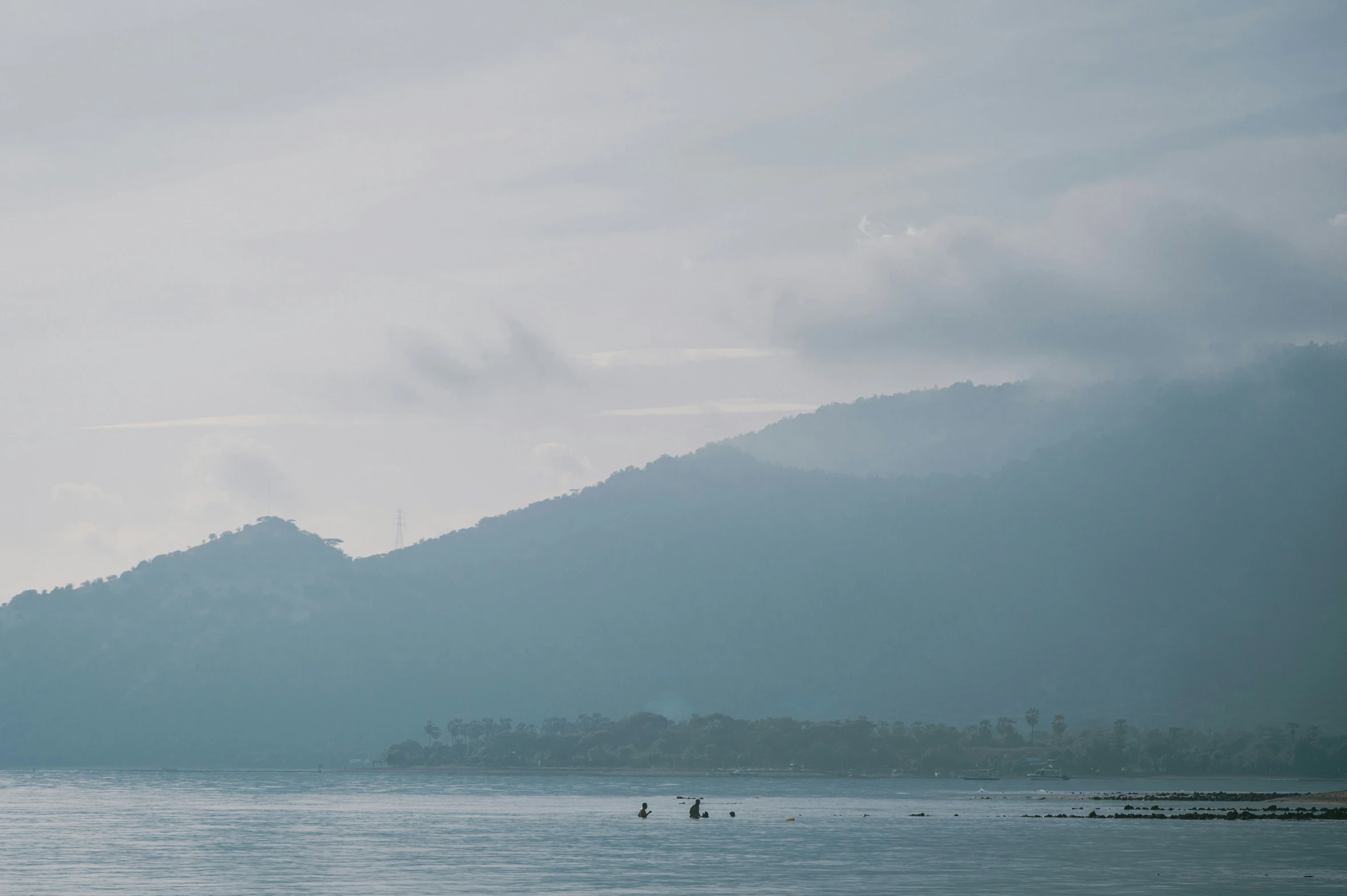 two people paddleboarding in the ocean with mountains in the background