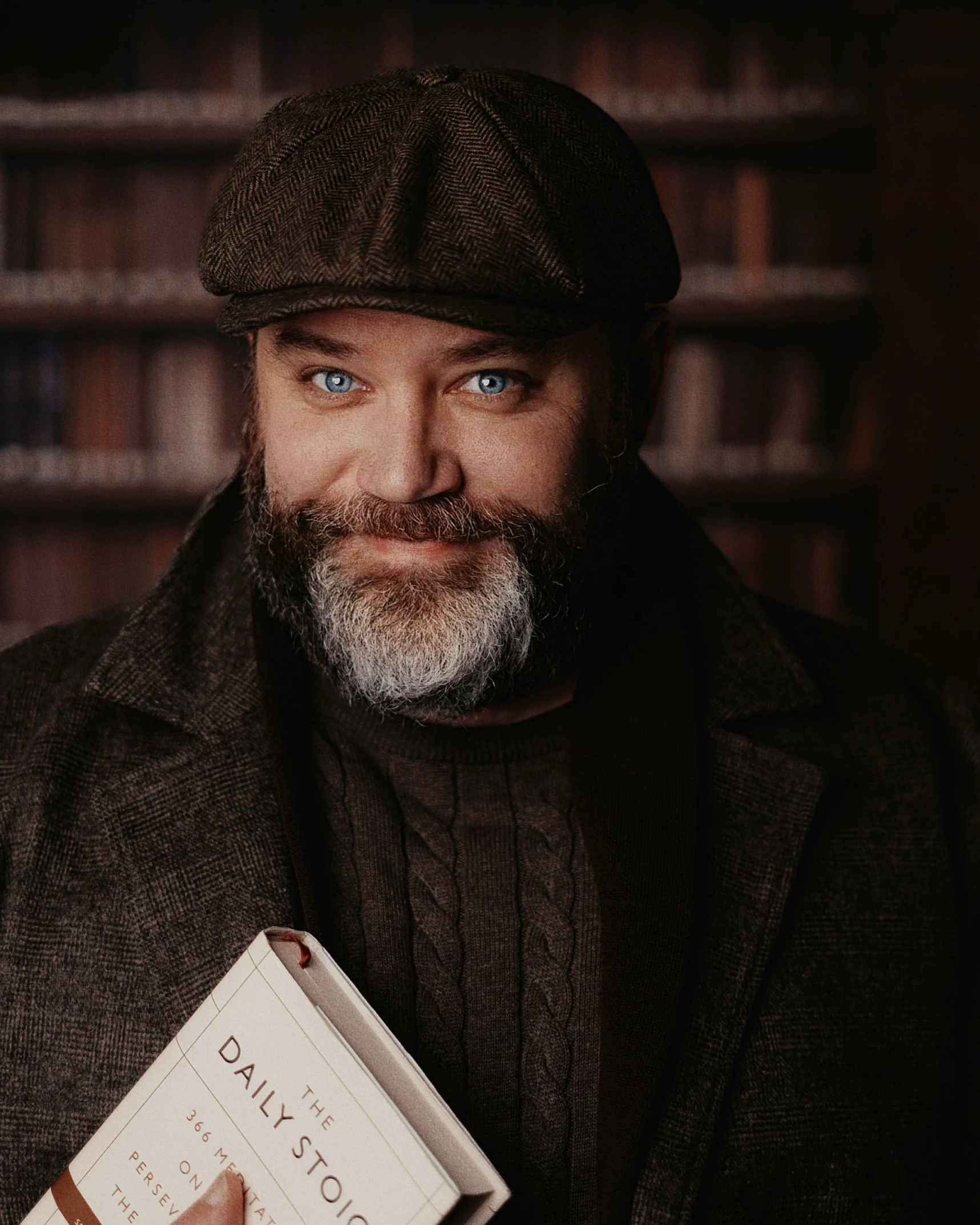 man holding book in the dark with bookshelves in the background