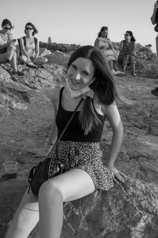 the young woman is sitting on a rock in front of a group of people