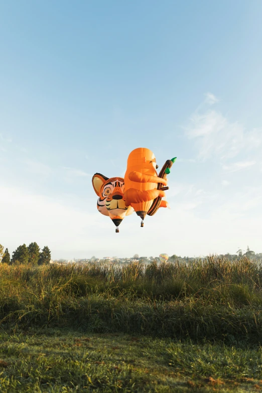 an orange and black balloon shaped like an animal flying in the sky