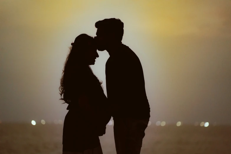 a couple in silhouette kiss each other in front of the sun