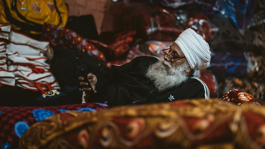 a old man with white turban sits amongst a rug