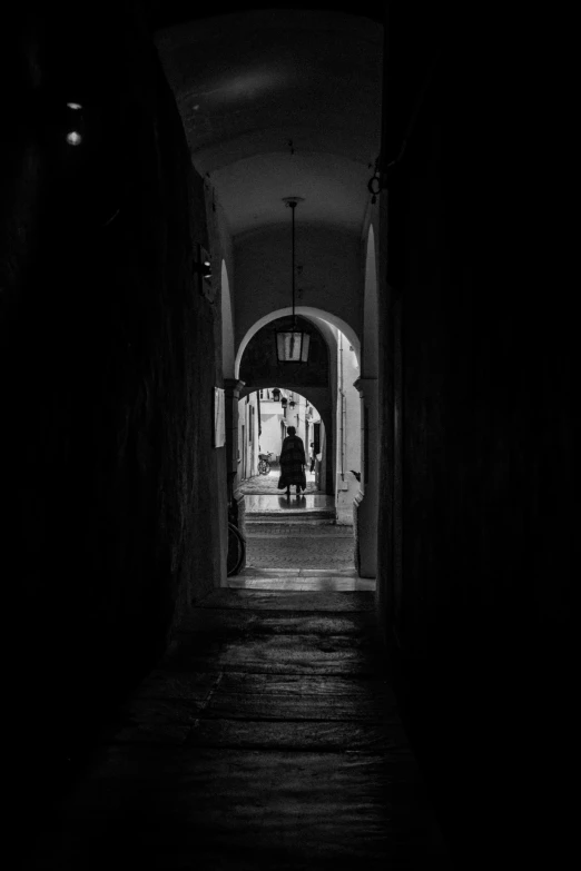 a person in black and white standing outside an archway at night