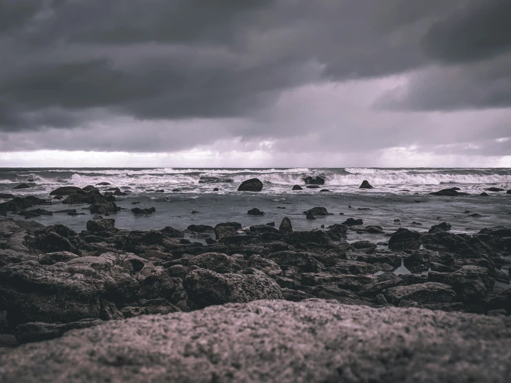 a stormy sky is over the ocean on a rocky beach