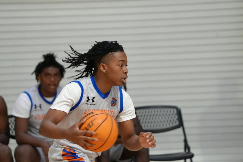 young woman wearing white and blue uniform holding a basketball