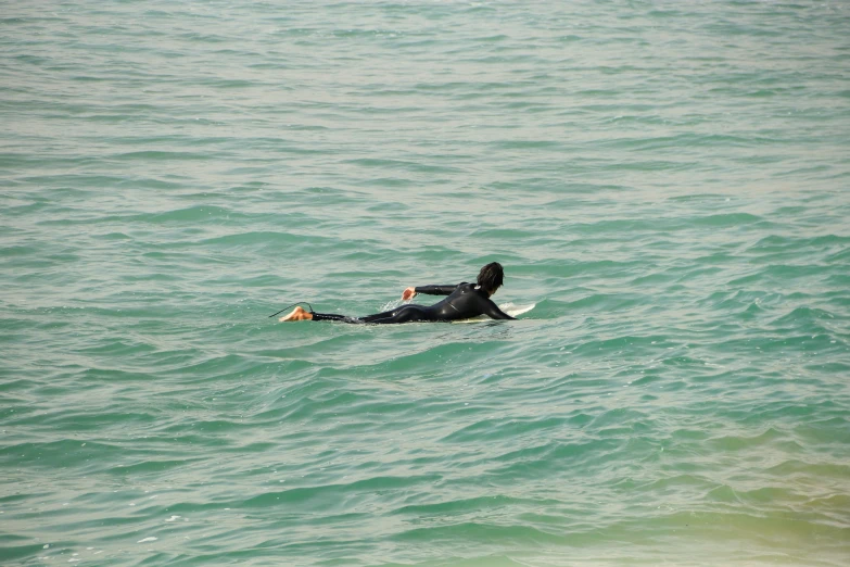 a surfer in the ocean wearing black riding on a surfboard