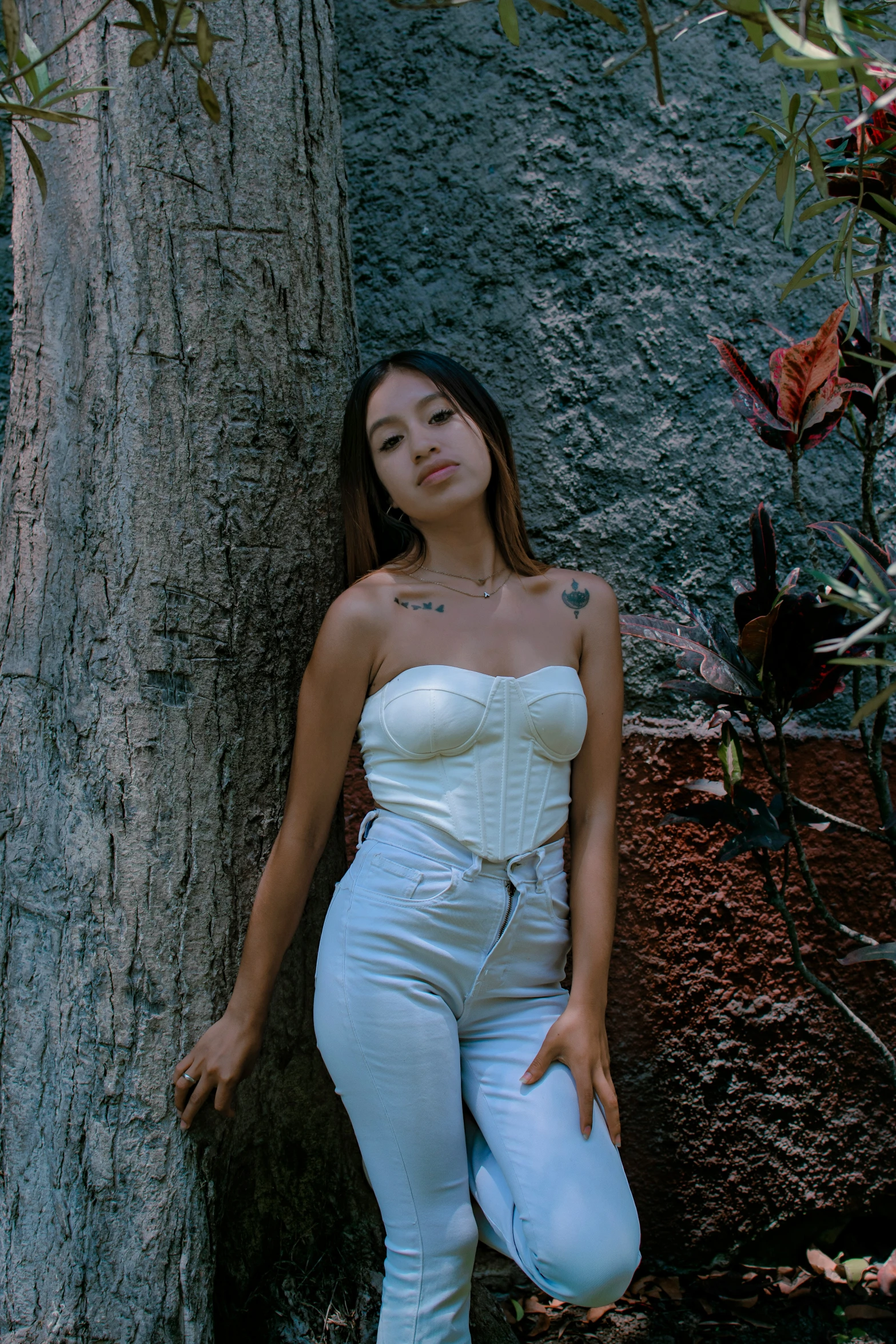 a woman with tattoos and white outfit standing next to a tree