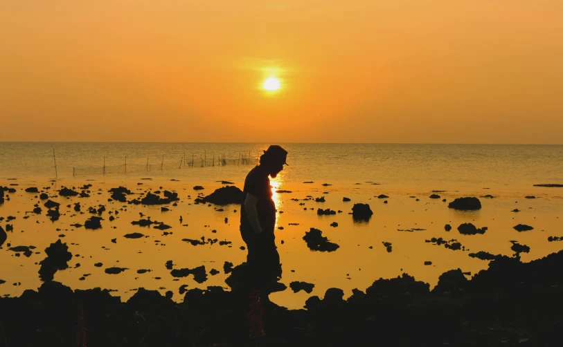 woman standing on a rocky shore at sunset