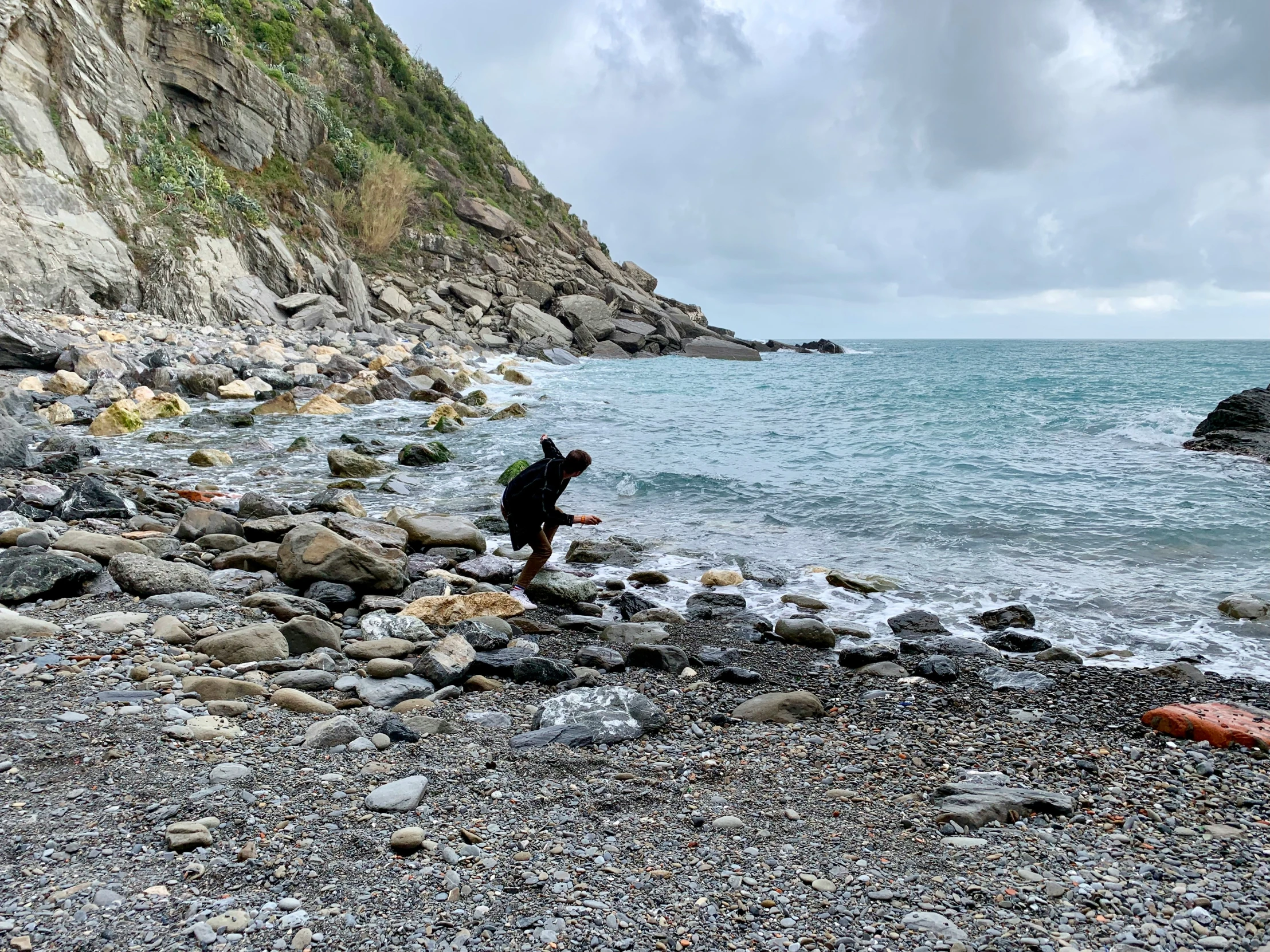 a person walks on a rocky beach with the ocean in the background