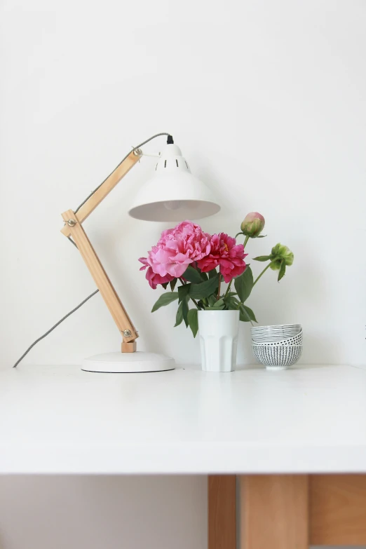 pink flowers in white vase on desk next to lamp
