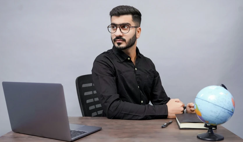 a man sitting at his computer with a globe in front of him