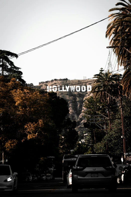 many cars are parked on the street under an hollywood sign