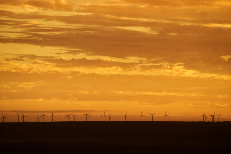 a large number of wind turbines in the distance with a orange sky