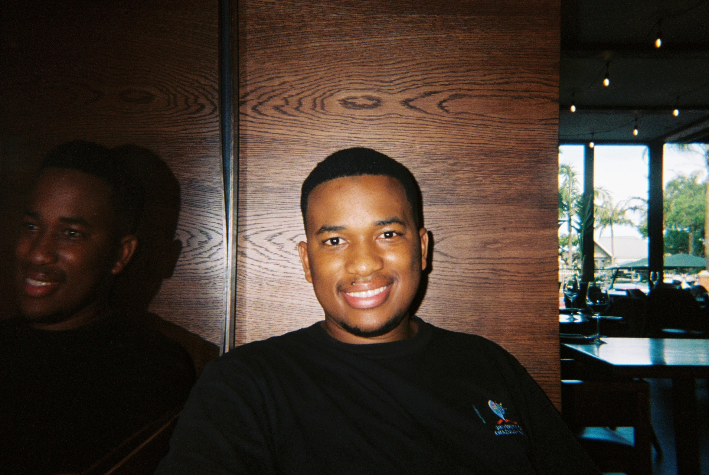 man with dark shirt smiling at camera in front of wooden wall