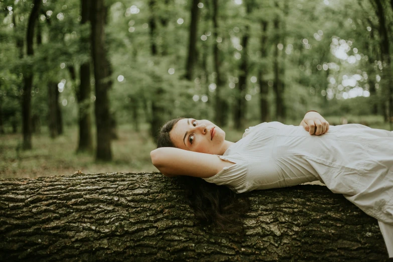 a girl laying on a tree looking off to her side