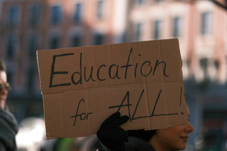 a man holds up a cardboard sign reading education for all