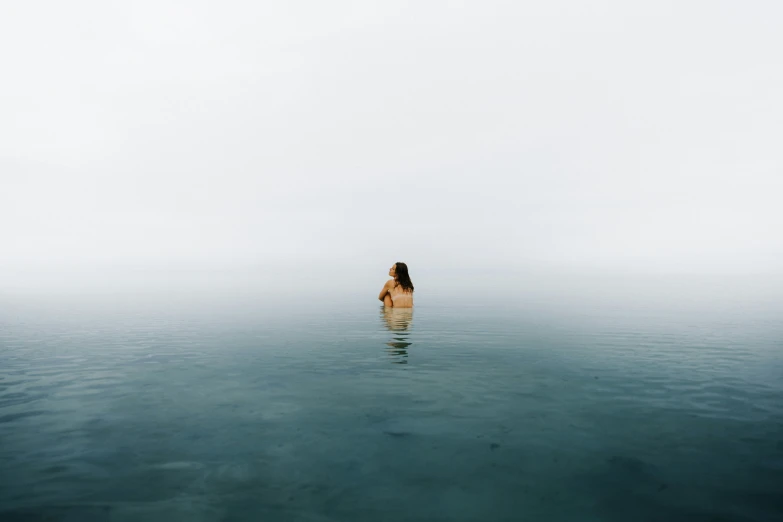 a woman is swimming in the water in front of a foggy sky