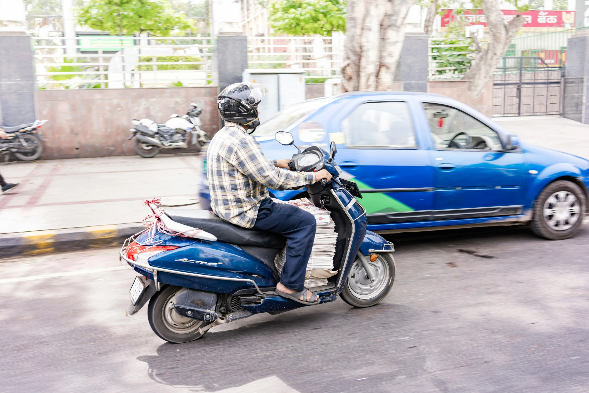 the person in jeans and a checked shirt is riding a motor scooter