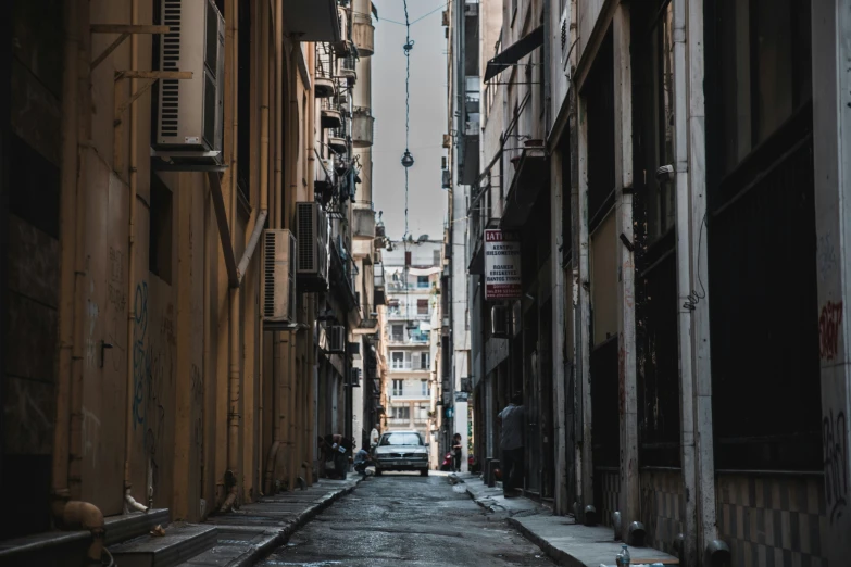 an alleyway with buildings, cars, and trash can in it