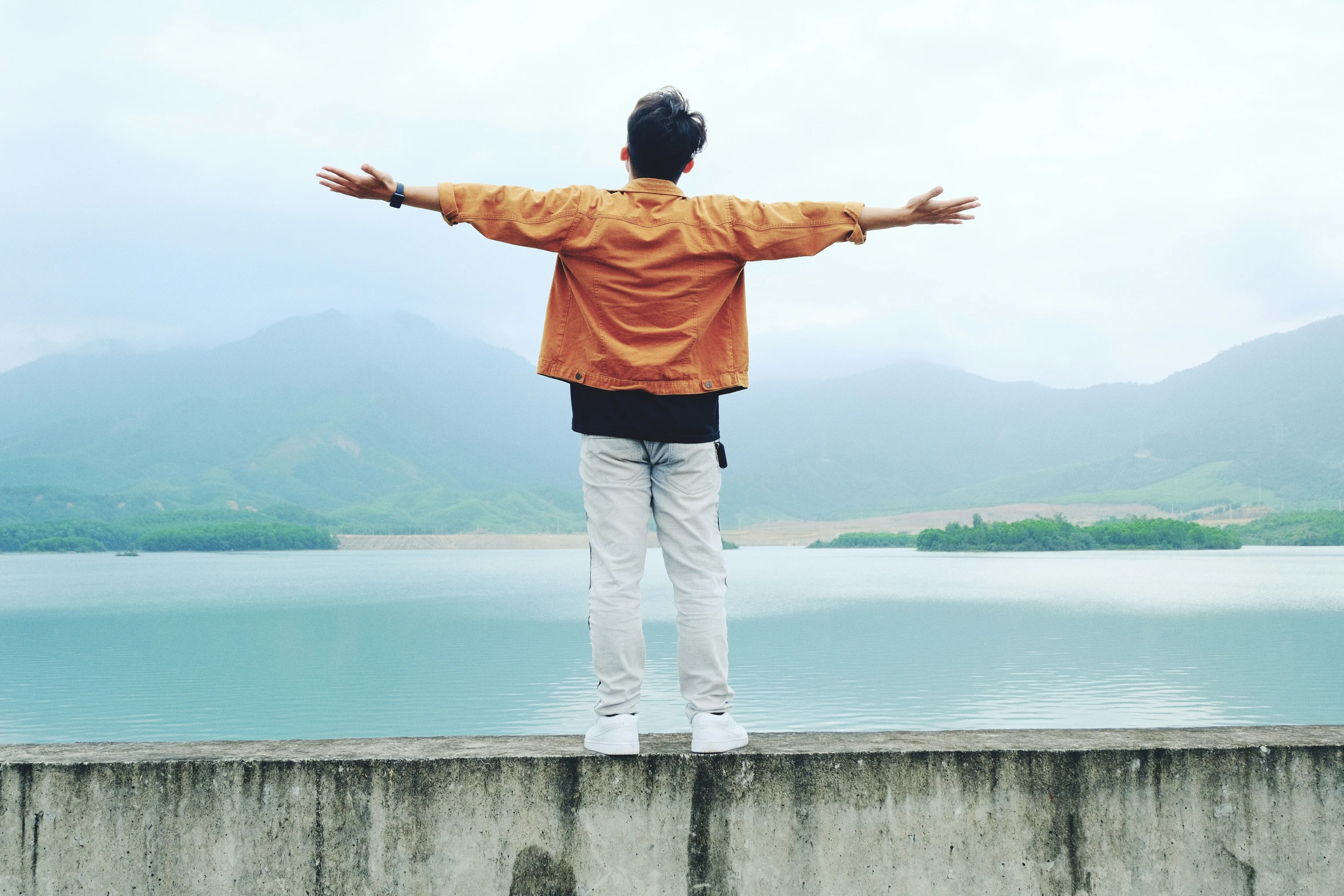 a man with his arms out standing on the edge of a lake