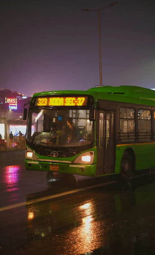 a green bus is traveling down the rain soaked road