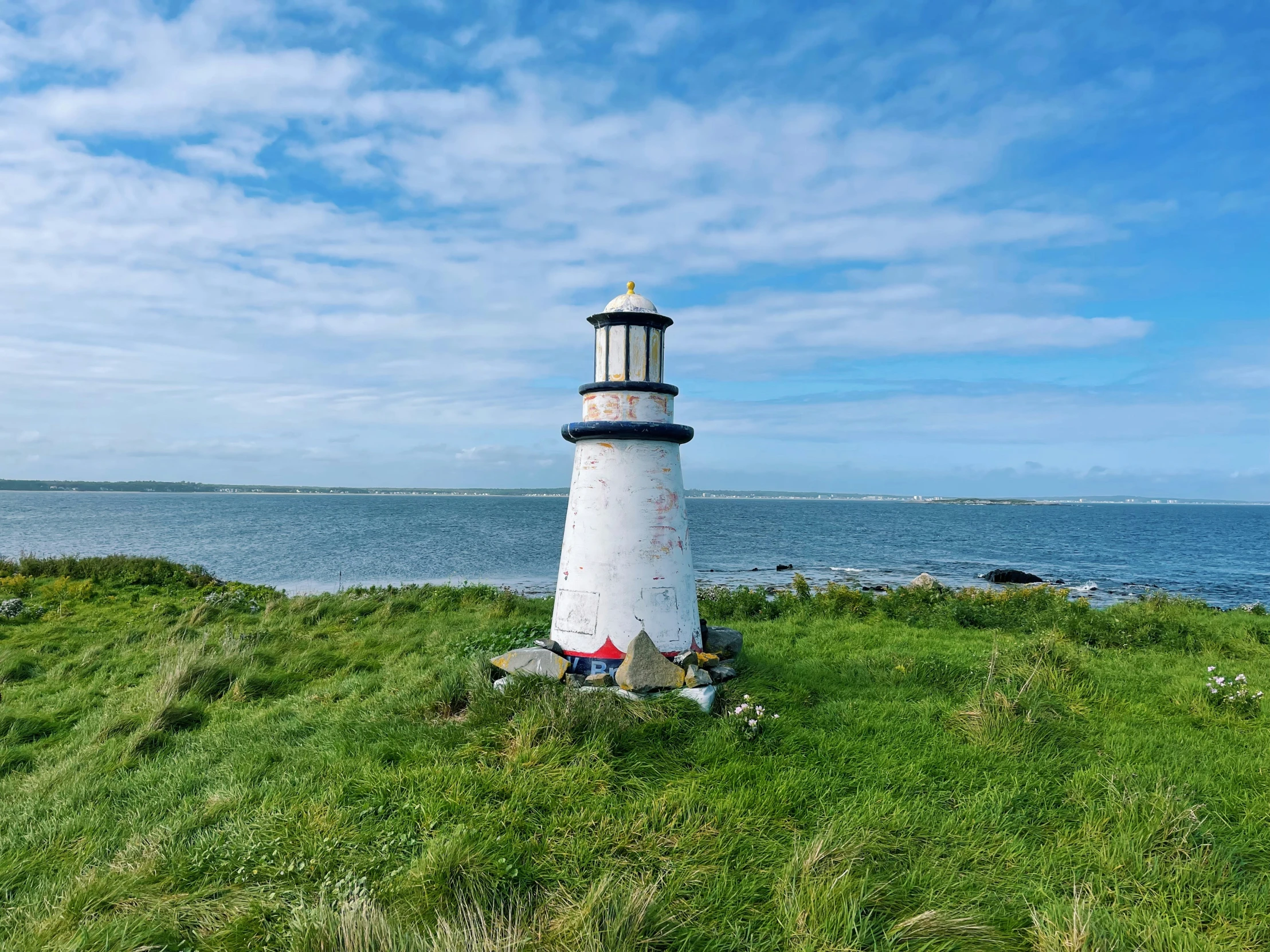 the tall light house is on top of grass near the water
