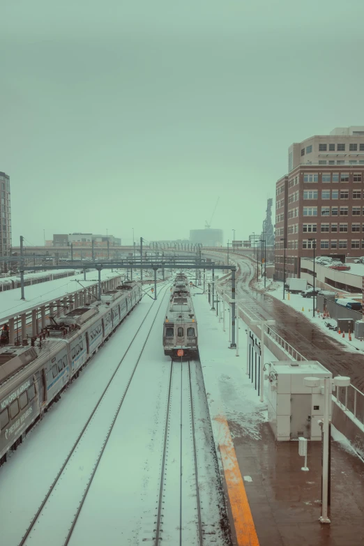 a snowy scene with trains parked on rails and a bench with people standing on it