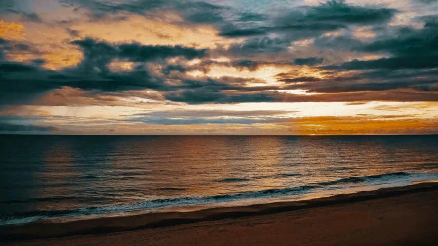 a long beach is next to a body of water with a sunset in the background