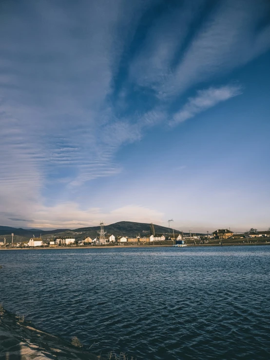 water has a blue sky, clouds and hills with a town in the distance