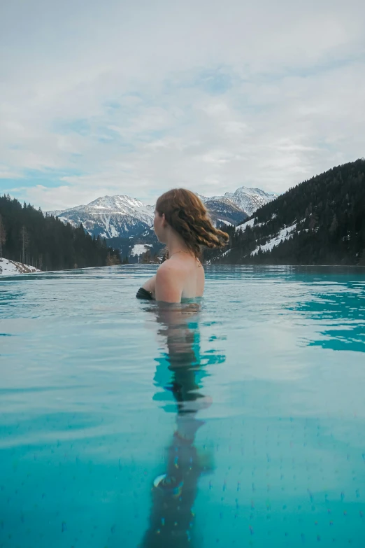 a woman is sitting in the water looking at a mountain