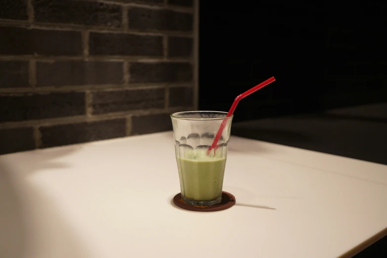 a green drink on a table with a red straw in it