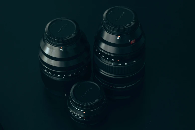 three black camera lenses side by side on a dark surface