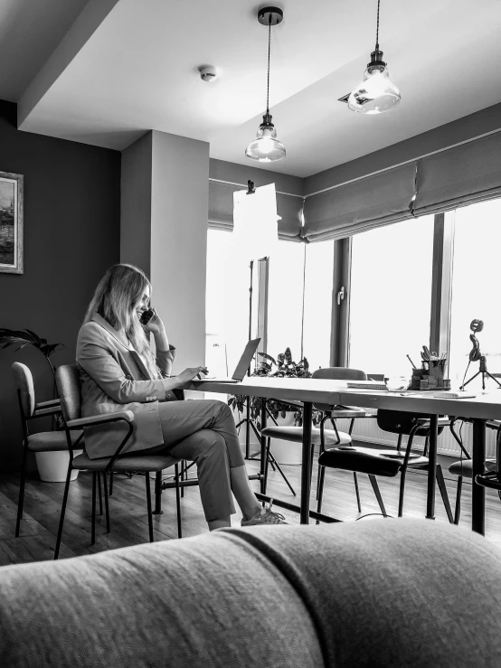 a woman with her back turned is sitting on a chair at a long table talking on the phone