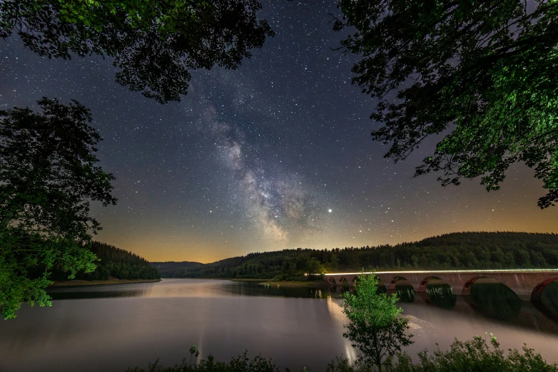 a view from the shore of a lake, with stars in the sky and the trees surrounding it