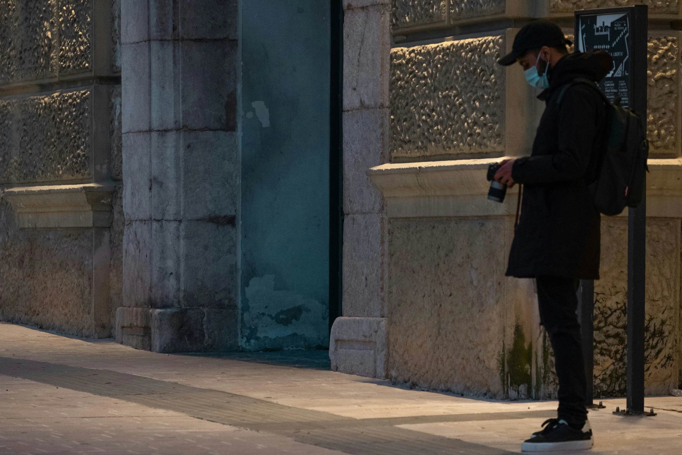 a man standing on the sidewalk wearing a mask and using his phone