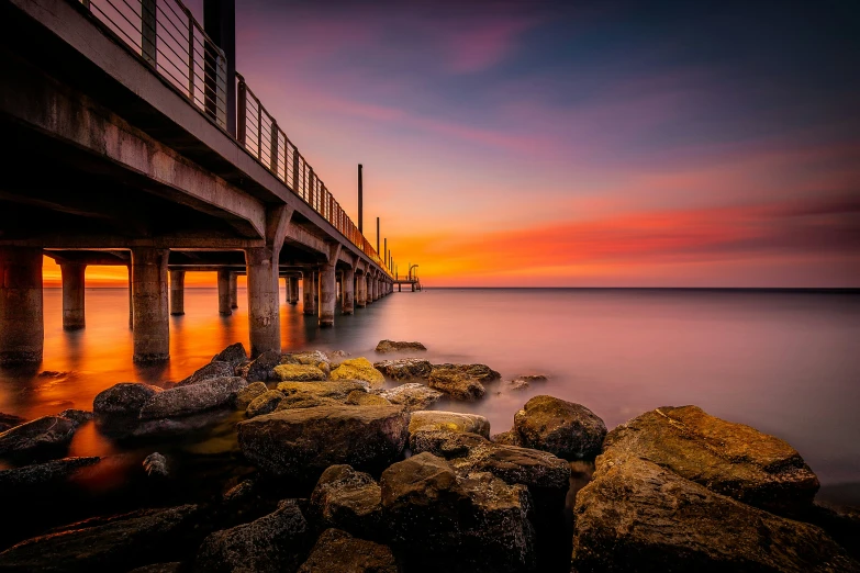 a view of a bridge over the ocean with rocks