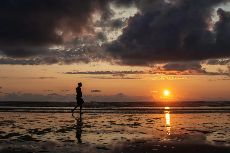 a woman running on the beach while the sun goes down