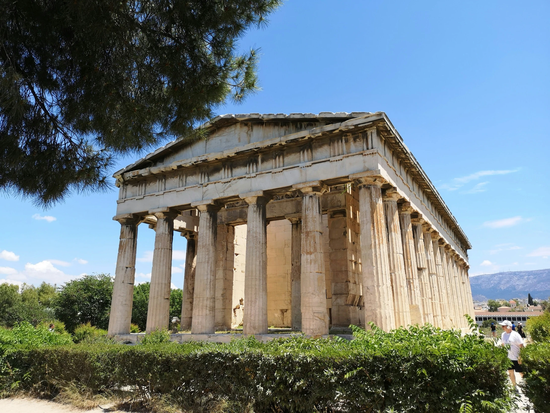 two people walk past an old greek style structure