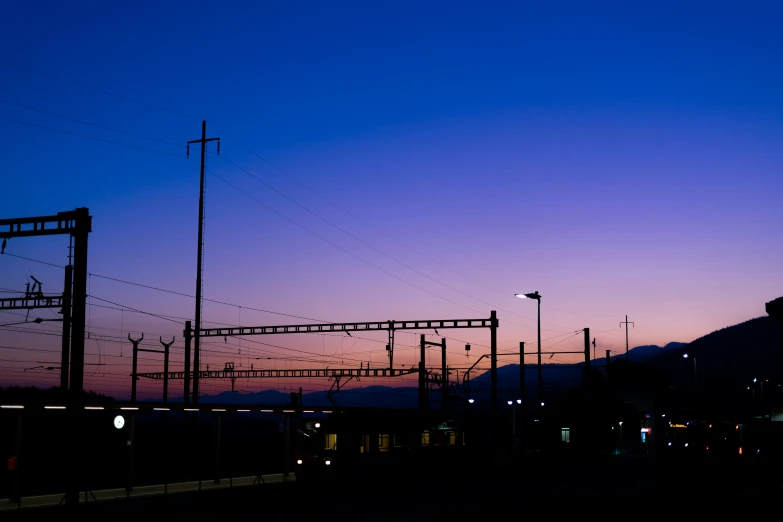 a train traveling under a purple sky with wires hanging over it