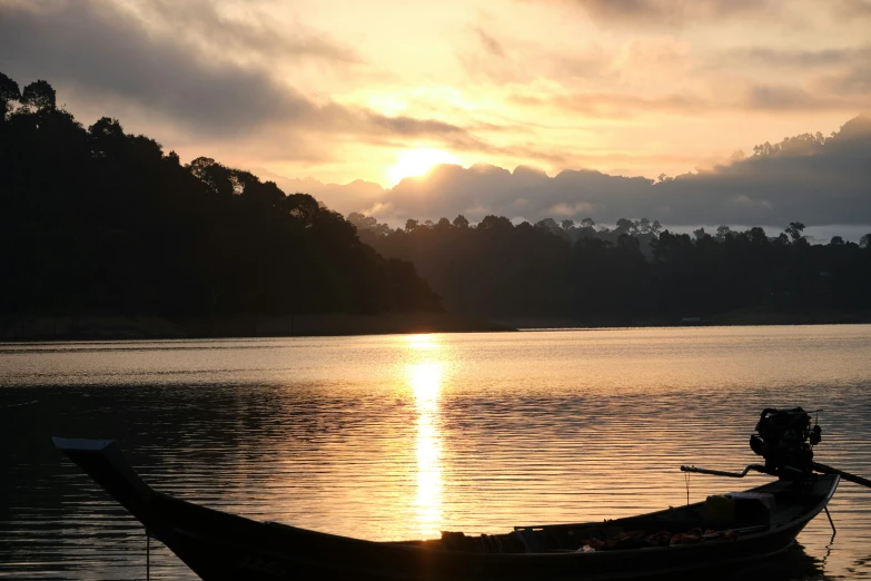 the sun rises on the horizon as a boat sits on the water