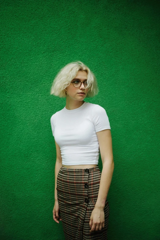 a young woman in a short skirt standing against a green background