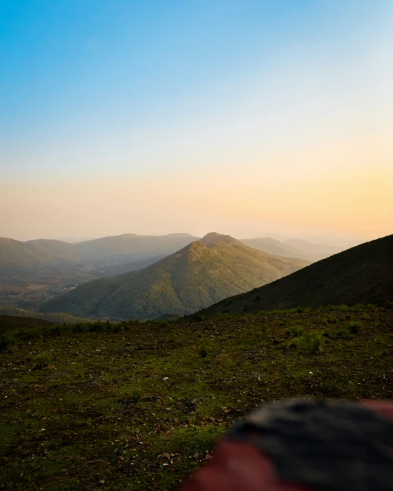 a mountain area with grass and trees with mountains behind