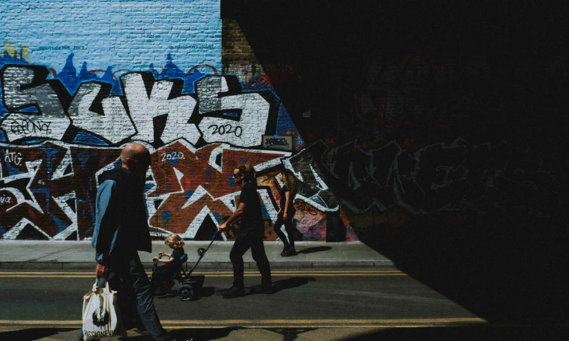 the people are walking down the street past some graffiti