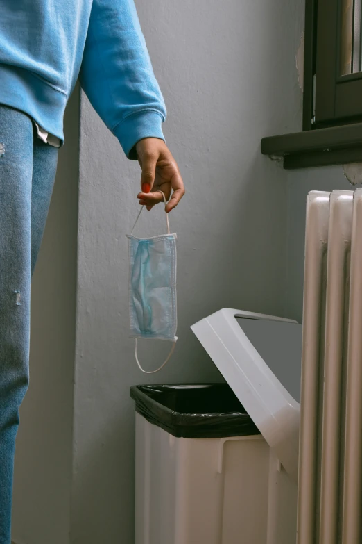 the person is holding a clear plastic bag next to a trash can