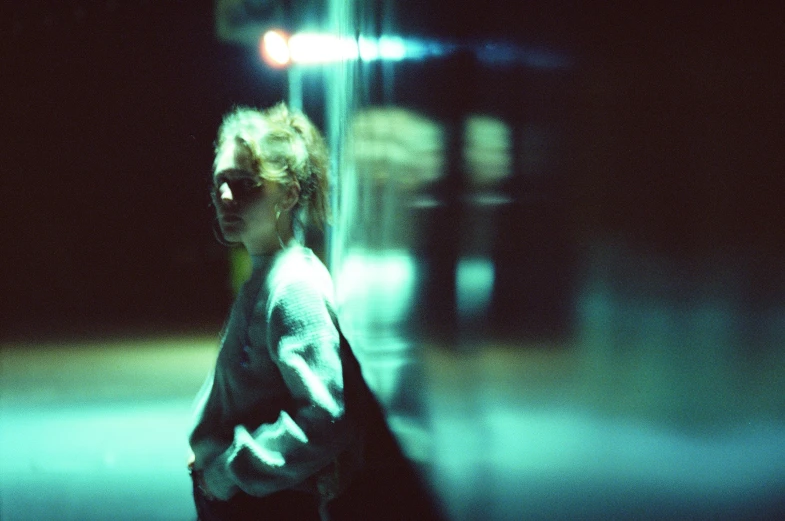 a blurry image shows a woman walking on the sidewalk at night