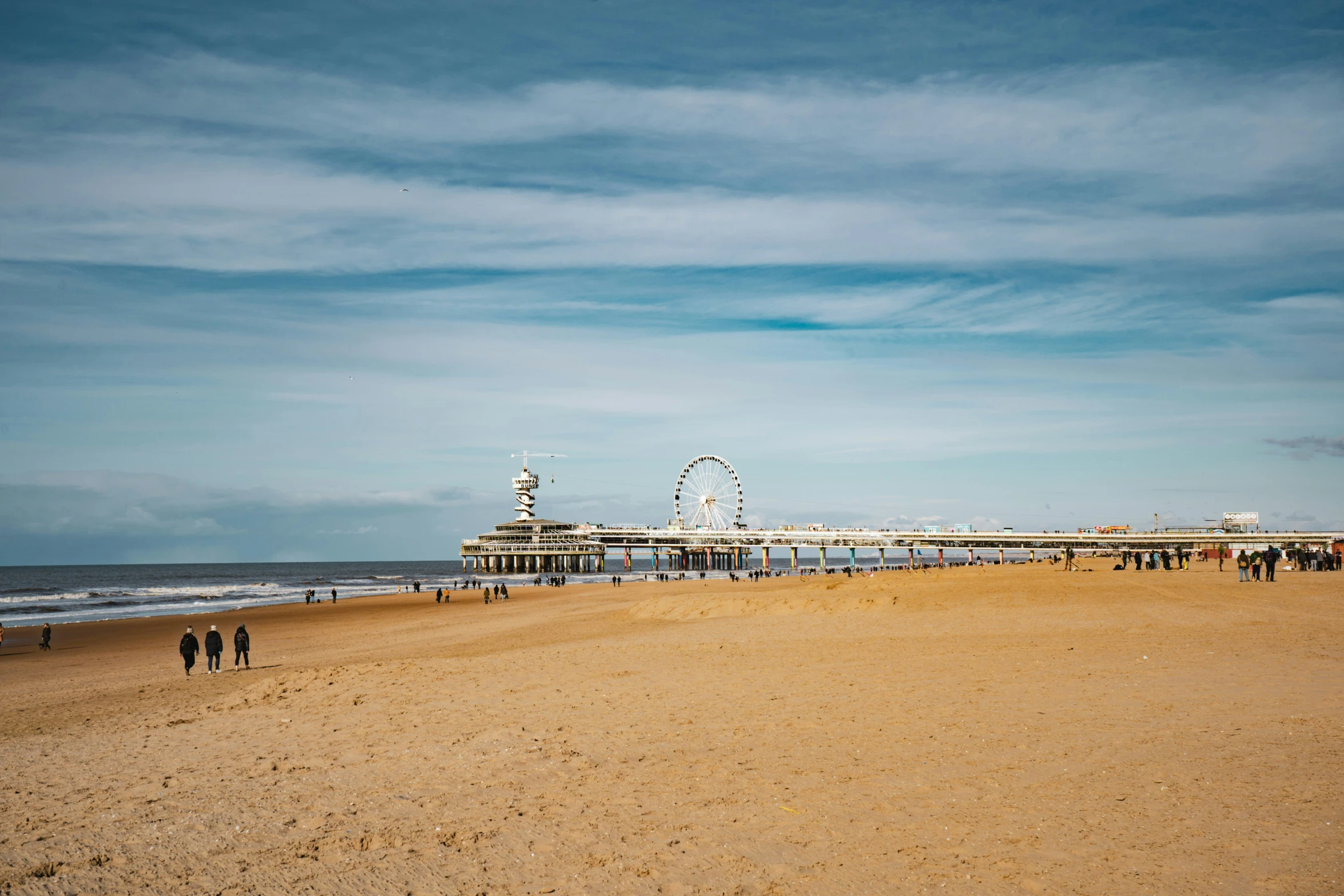 people on a beach by an ocean under a pier