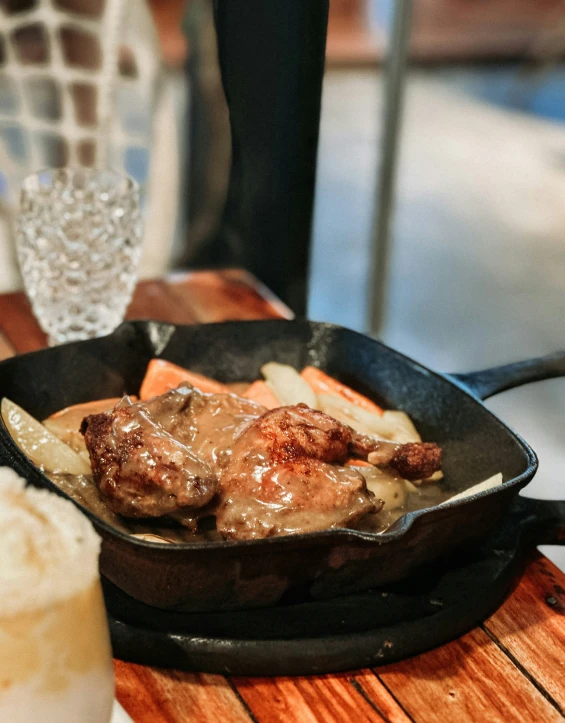 an iron set filled with beef and potatoes sitting on top of a wooden table